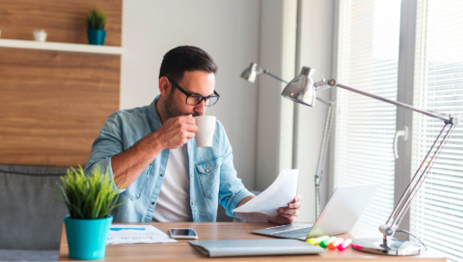 A man at his desk, drinking coffee and reviewing taxes